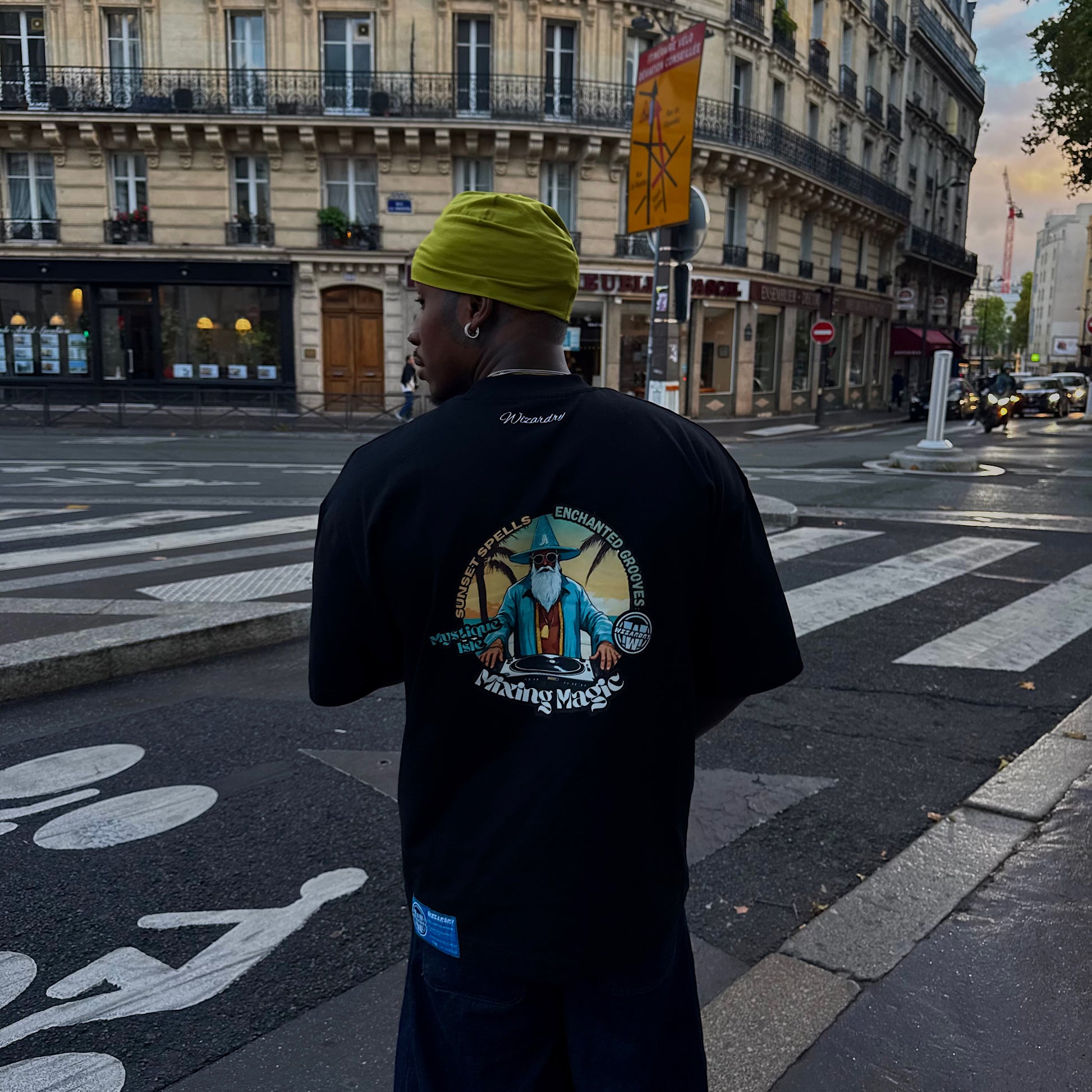 Model wearing the Wizardry Mixing Magic oversized heavyweight black graphic T-shirt with ‘Mixing Magic’ back print, italic ‘Wizardry’ neck embroidery and blue woven label
